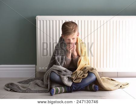 Sad Little Boy Suffering From Cold On Floor Near Radiator