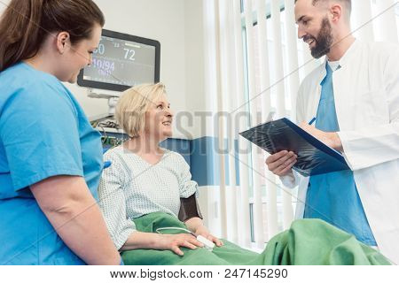 Doctor and nurse talking to patient in recovery room of hospital after she woke up from operation 