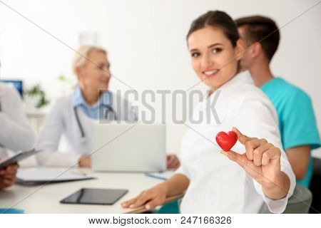 Female Doctor Holding Small Heart At Table In Clinic. Cardiology Conference
