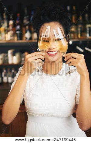 Smiling Young Woman Hlding Two Champagne Glasses In Front Of Her Face