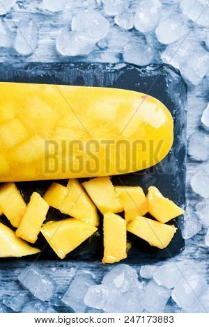 high anble shot of a homemade ice pop made with natural pineapple or mango, on a natural slate tray surrounded by ice