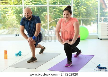 Overweight Man And Woman Doing Exercise On Mats In Gym