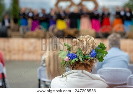 A Woman With A Flower Crown In Her Head Is Watching A Concert. View From The Back.