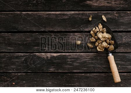 Gold Ore Nuggets In Shovel On Old Adventurer Table. Goldminer Treasure Hunter Concept.