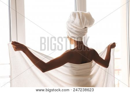 Back view of an attractive african woman wrapped in a towel standing in front of the wondow