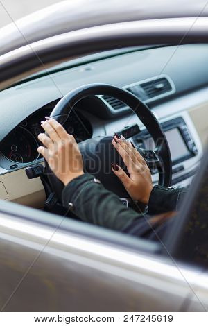 Girls Hands Are Aestetically Situated On The Black Steering Wheel In A Grey Car.