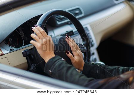 Girls Hands Are Aestetically Situated On The Black Steering Wheel In A Grey Car.