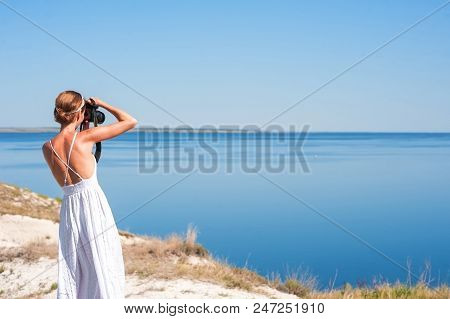 A Girl In A White Sarafan Stands And Takes Pictures Of The Beautiful Nature Of Rocks And Water. Clif