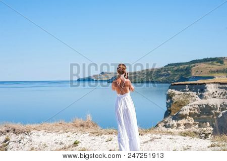 A Girl In A White Sarafan Stands And Takes Pictures Of The Beautiful Nature Of Rocks And Water. Clif