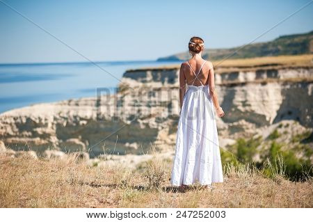 A Girl In A White Sarafan Stands And Takes Pictures Of The Beautiful Nature Of Rocks And Water. Clif