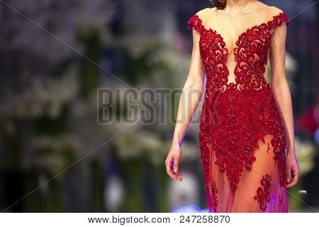 Female Model Walks The Runway In A Red Dress During A Fashion Show. Fashion Catwalk Event Showing Ne