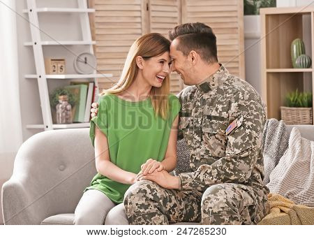 Young Man In Military Uniform With His Wife On Sofa At Home