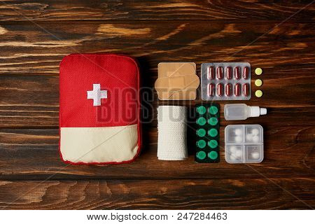 Top View Of First Aid Kit Composed With Various Pills And Bandage On Wooden Tabletop