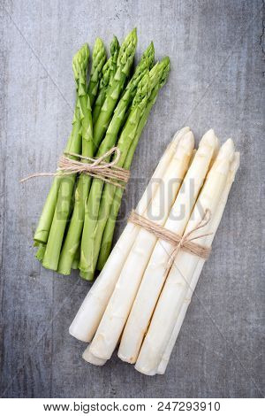 Row green and white asparagus bunch as top view on a gray board 