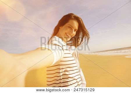 Cheerful brunette woman wallking on the beach, leading camera towards her