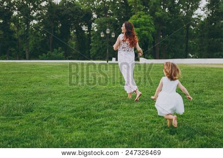 Little Cute Child Baby Girl Running Catching Up Have Fun With Joyful Woman In Light Dress On Green G