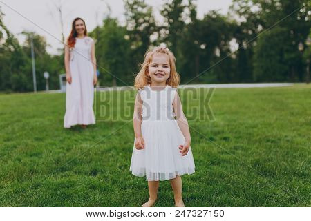 Smiling Little Cute Child Baby Girl In Light Dress Walking, Play And Have Fun On Green Grass Lawn In