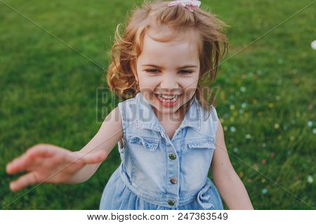 Smiling Little Cute Child Baby Girl In Denim Dress Pointing Hand On Camera, Have Fun On Green Grass 