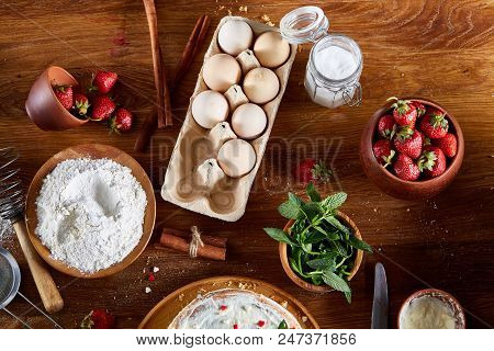 Strawberry Tart Covered With Whipped Sour Cream Surrounded By Organic Ingredients Over Wooden Backgr