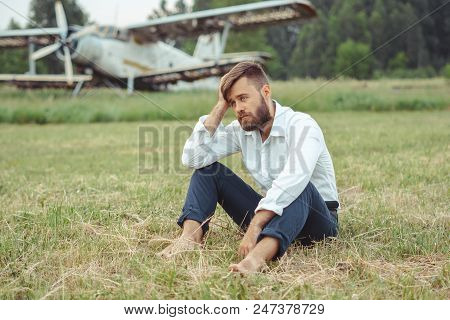 A Man In A Shirt Sitting On The Grass At The Old Plane