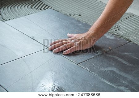 Worker placing ceramic floor tiles on adhesive surface