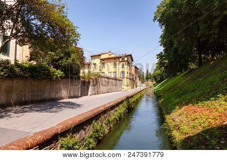Lucca old town cityscape with canal along narrow street and fortified city wall, Tuscany, Italy