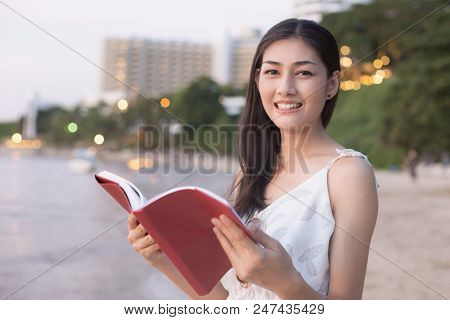 Asain Woman Reading Book At Beach, Woman Holding Book With Attractive Smiling.