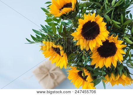 Bouquet Of Bright Sunflowers With Gift On A White Table.