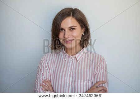 Close Up Portrait Of Smiling European Woman On Gray Background. She Is Crossing Hands And Looking Wi