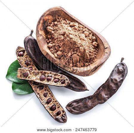 Carob pods and carob powder in the wooden bowl. White background.