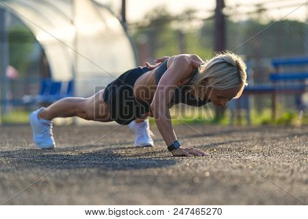 Young Attractive Blonde Woman Doing Push Ups Outdoors At Sunsut Light