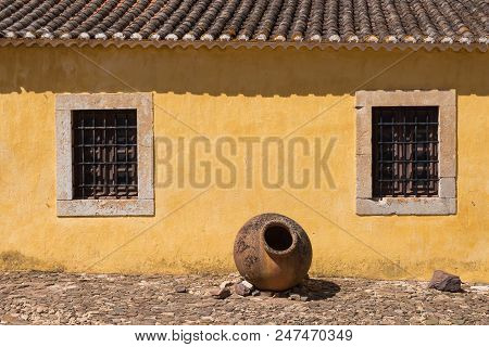 Yellow Wall Of An Old House, Part Of Castro Marim Castle. Windows With Stone Frames And A Grating. T