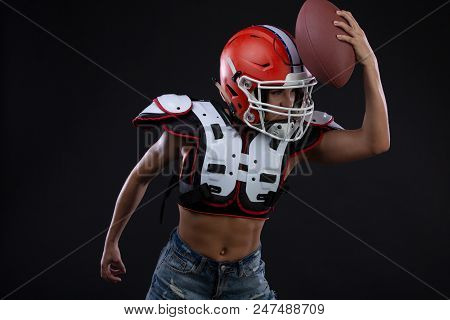 Sportive Serious Woman In Helmet Of Rugby Player Holding Ball In Stuio On Black Background. Gender E
