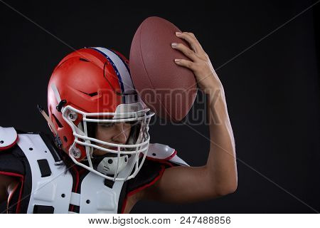 Sportive Serious Woman In Helmet Of Rugby Player Holding Ball In Stuio On Black Background. Gender E