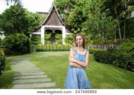 Young Girl Wearing Jeans Sundress And Standing On Green Grass Near Resort House. Concept Of Summer V