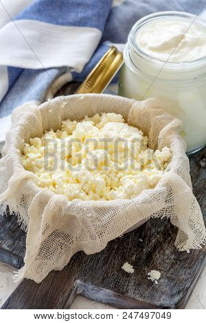 Fresh Cottage Cheese In A Bowl Of Cheesecloth And Jar Of Sour Milk On A Table With Linen Cloth.