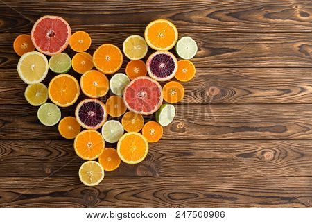 Overhead View Of Different Fresh Fruit Arranged In Shape Of Love Heart On Brown Wooden Background.