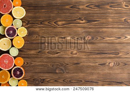 Assorted Cut Fresh Ripe Citrus Fruit Formed Into A Side Border On A Textured Wood Background With Co
