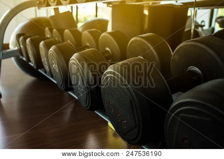 Dumbbells Lie In A Row On The Inventory Rack In The Gym Or Fitness Center  Background.