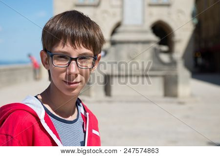 Young boy spectacled looking at camera outdoor over San Marino city-state. Vision, eyesight, sight, diopters, spectacles, glasses, health.