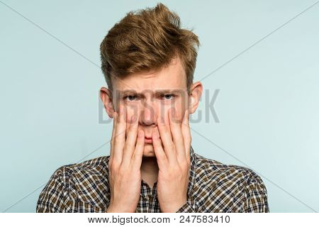 Sad Rueful Depressed Cheerless Man Covering His Face In Hands. Portrait Of A Young Guy On Light Back