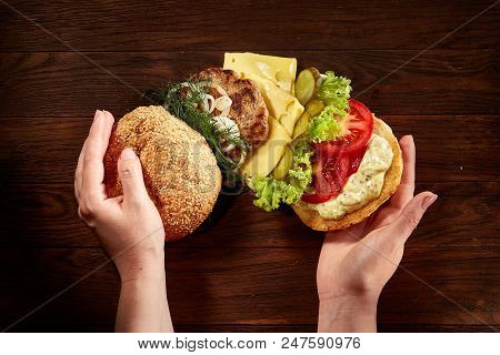 Woman's Hands Holding Traditional American Burger On Wooden Background, Top View, Close-up.