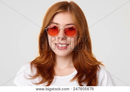 Positive Lovely Fashionable Young Woman With Gentle Smile, Wears Red Trendy Sunglasses, Being In Goo