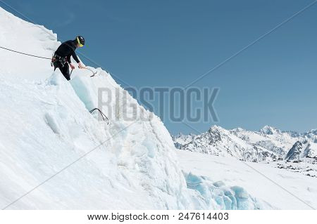 A Professional Mountaineer In A Helmet And Ski Mask On Insurance Makes A Nick-hole In The Glacier Ag