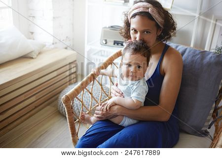 Indoor Shot Of Charming Young Latin Mother Wearing Elegant Blue Dress Enjoying Leisure Time With Tod