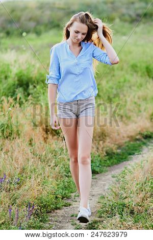 Happy Smiling Young Girl In Blue Shirt And Shorts In The Field