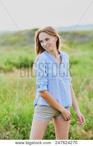 Happy Smiling Young Girl In Blue Shirt And Shorts In The Field
