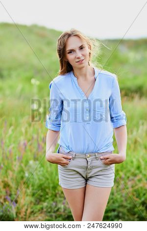 Happy Smiling Young Girl In Blue Shirt And Shorts In The Field