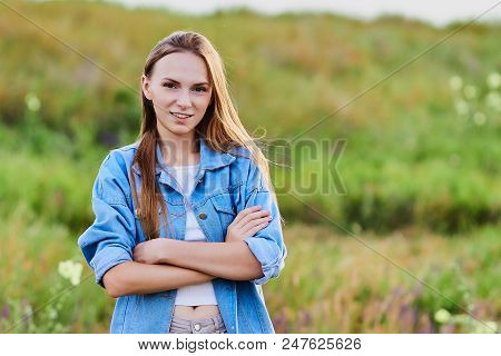 Happy Smiling Young Girl Wearing Blue Jeans Jacket And Shorts Is Standing In The Field