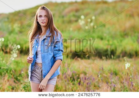 Happy Smiling Young Girl Wearing Blue Jeans Jacket And Shorts Is Standing In The Field